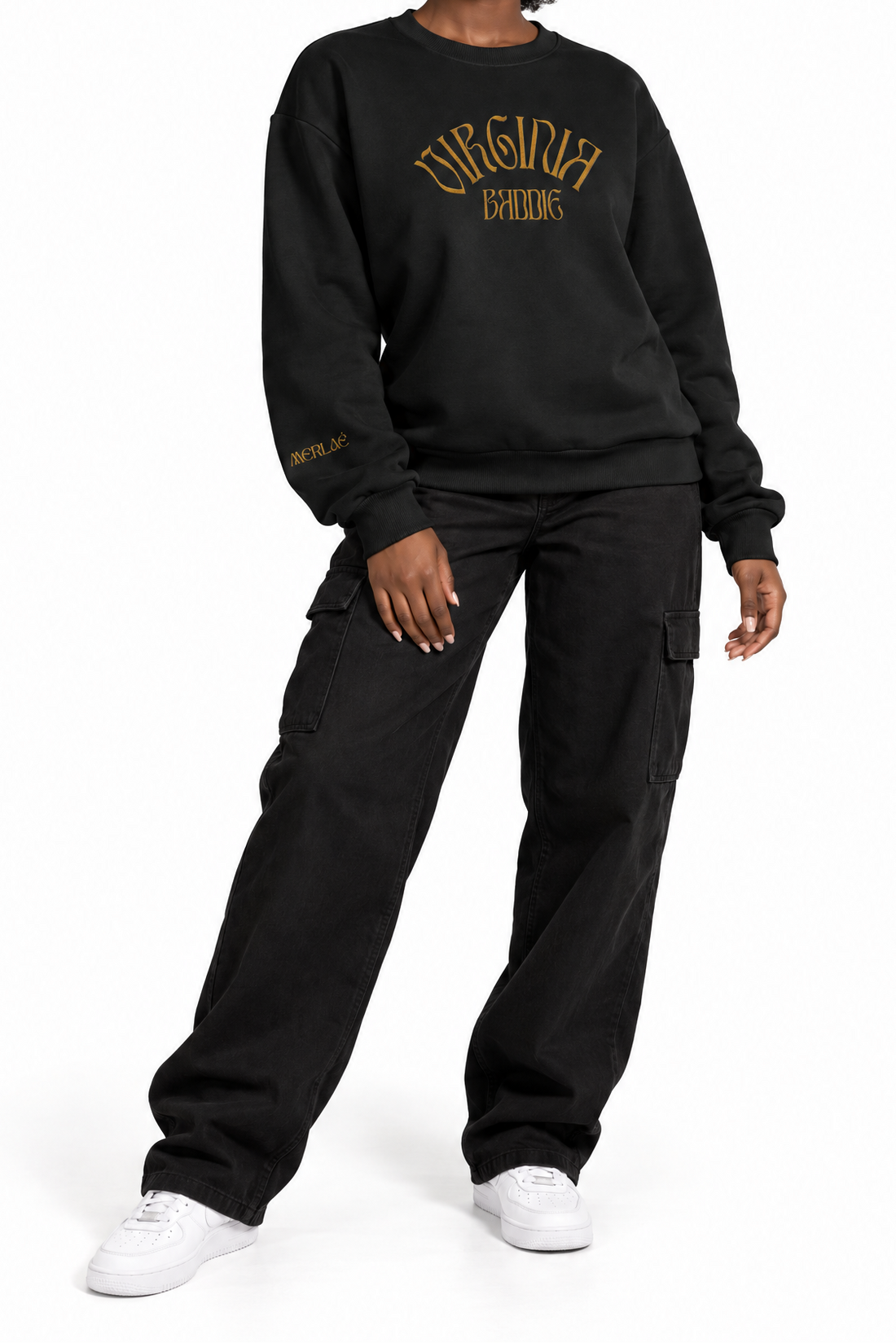 A model wearing a black crewneck sweatshirt with gold 'Virginia Baddie' text on the chest, paired with black cargo pants and white sneakers, against a plain white background.